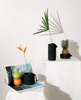 3 sizes of handcrafted holders/baskets hold clear glass vases with a pineapple inside displayed on white stand in white bright studio for product shoot