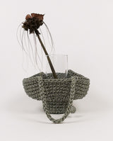 hand-crocheted bucket bag made from reflective paracord sits in the studio with a glass vase carried wild bat flower freshly cut from the garden