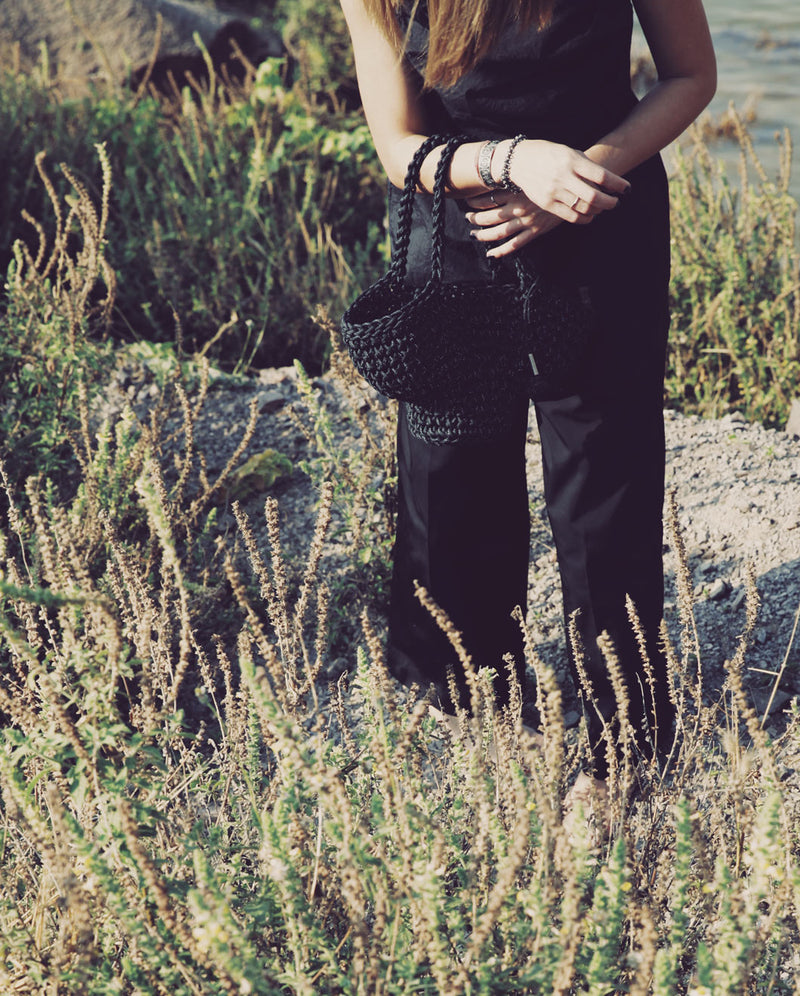 a lady with contemporary black outfit overlooking wild flowers along the river carrying her favorite jet black bucket bag